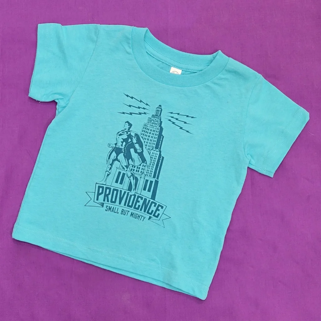 A turquoise t-shirt featuring a superhero graphic and "Providence: Small But Mighty" text.