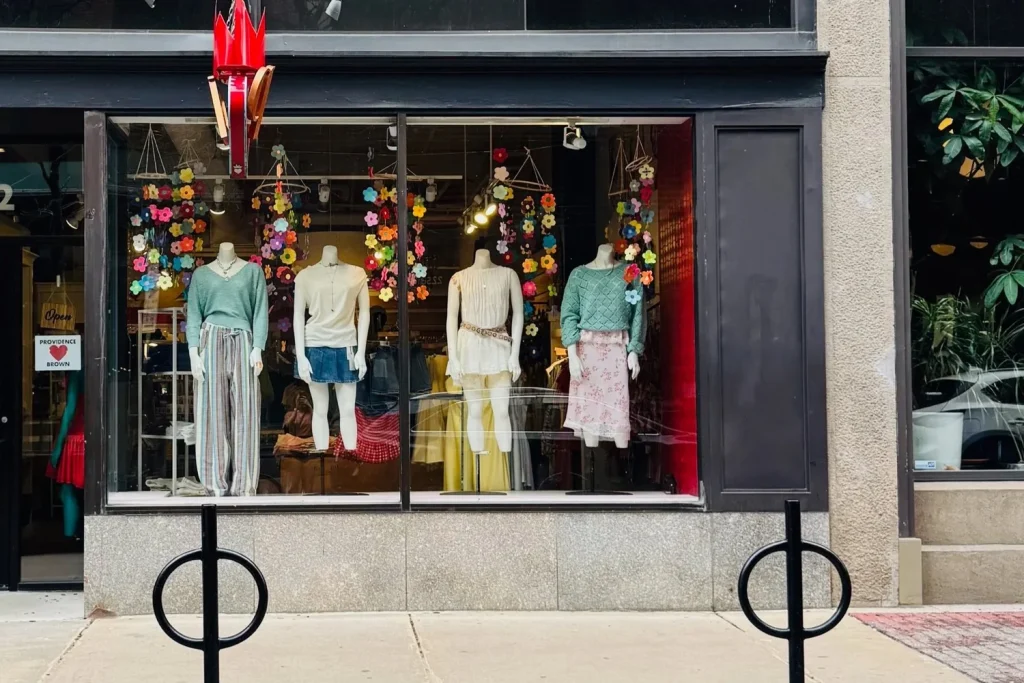 Storefront display features mannequins in various outfits, surrounded by colorful flower decorations.