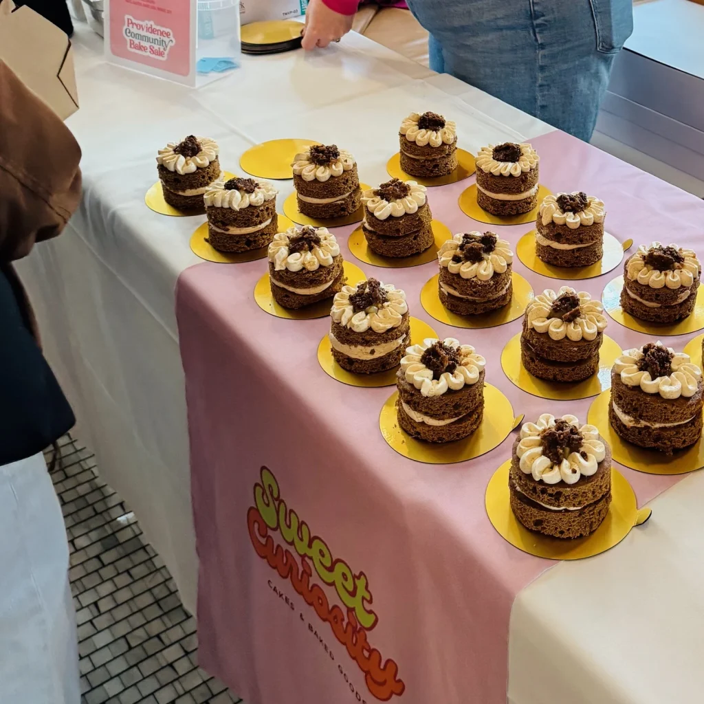 A table displays multiple small layered cakes with cream and toppings, labeled "Sweet Curiosity.