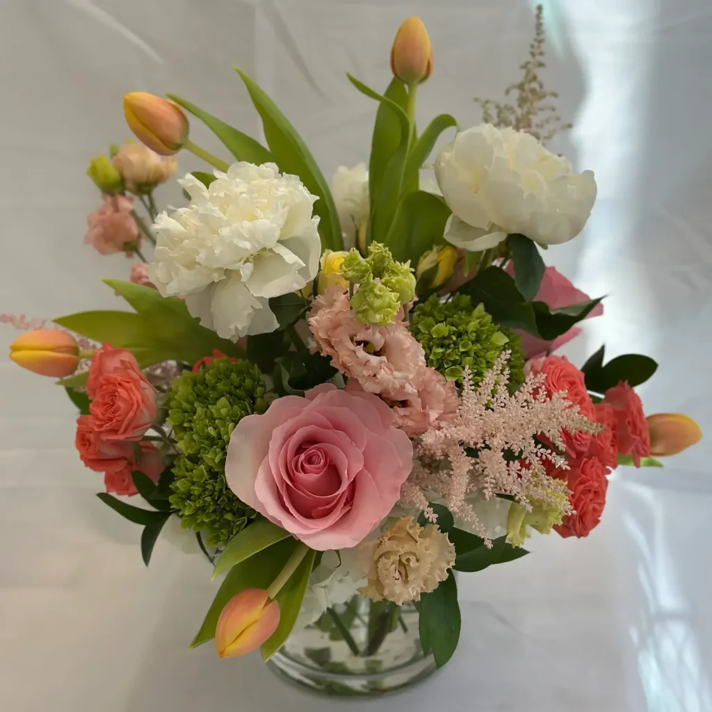 A vibrant floral arrangement featuring pink roses, white peonies, and green accents in a glass vase.