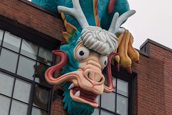 A colorful dragon sculpture with exaggerated features protrudes from a brick building.