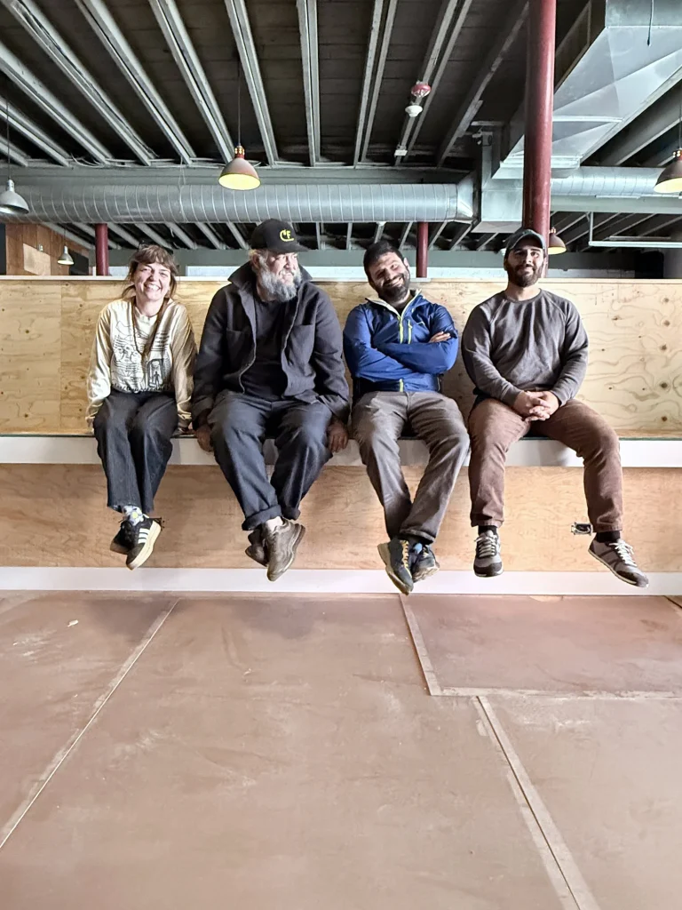 Four people sit on a ledge, smiling and relaxed, in a spacious, unfinished interior.