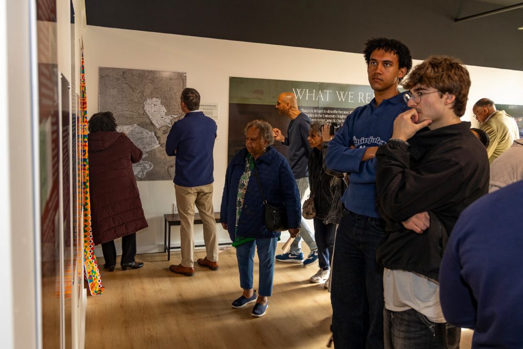 Visitors observe a map exhibit in a gallery, engaging in conversation and reflection.
