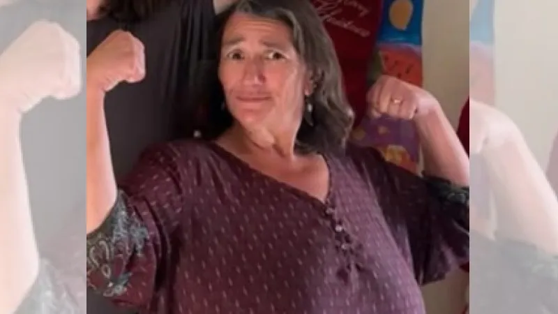 A woman flexes her arm muscles confidently, smiling at the camera.